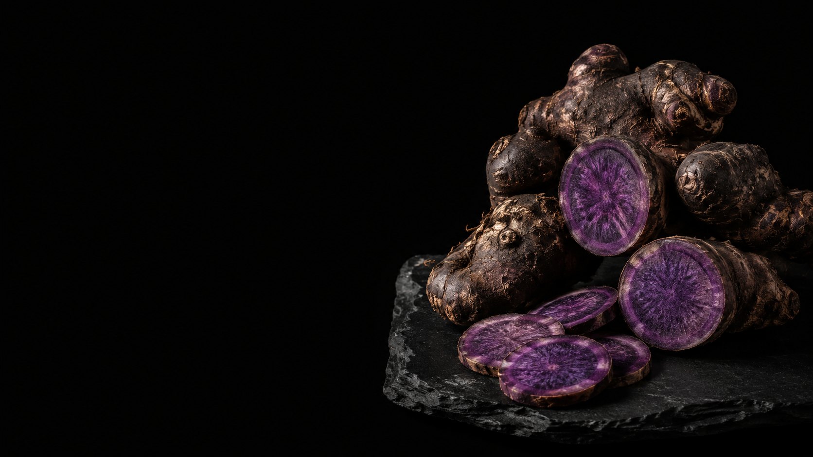 Black ginger rhizome on slate, sliced open to show the deep purple flesh